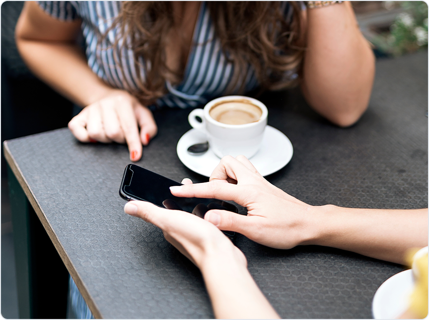 Two people at a café table looking at a phone over a cup of coffee