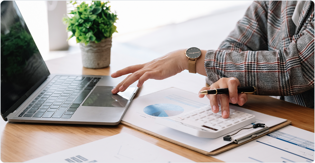 Hands working on a laptop and calculator next to a financial report with a pie chart