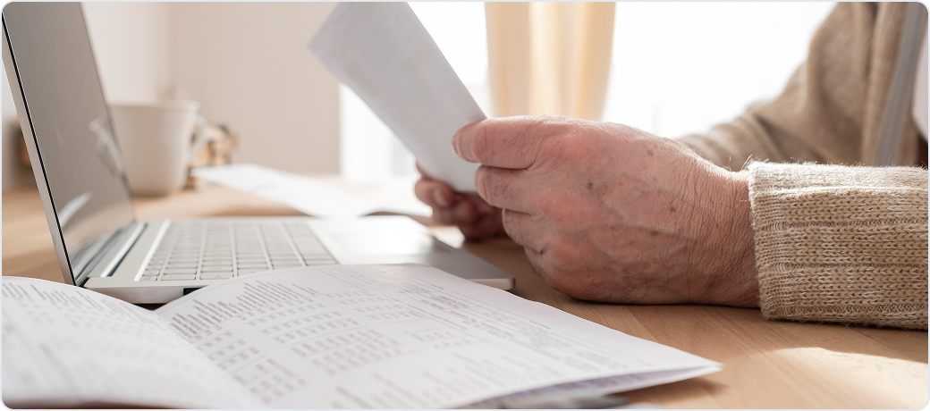 Hands holding a printed statement beside a laptop and an open ledger