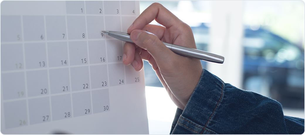 Hand with a pen pointing at dates on a calendar