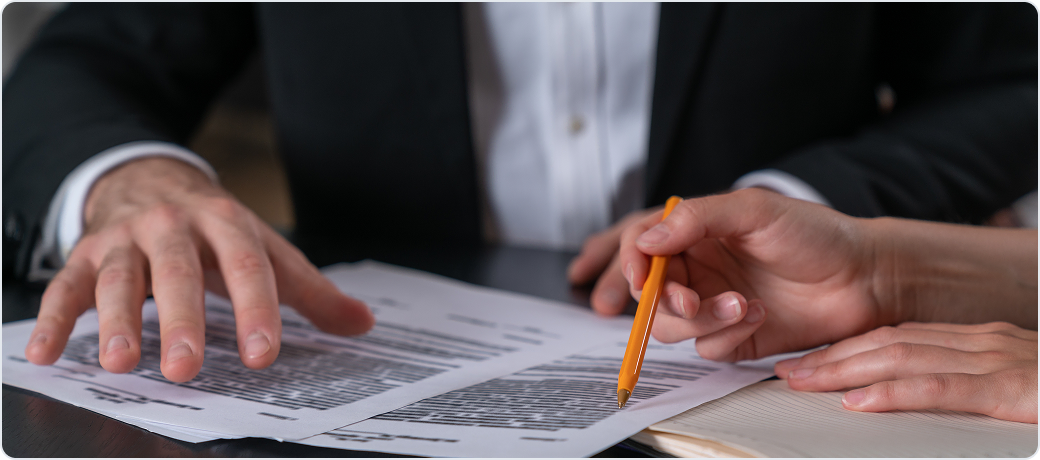 Two people reviewing a printed document line by line with a pen
