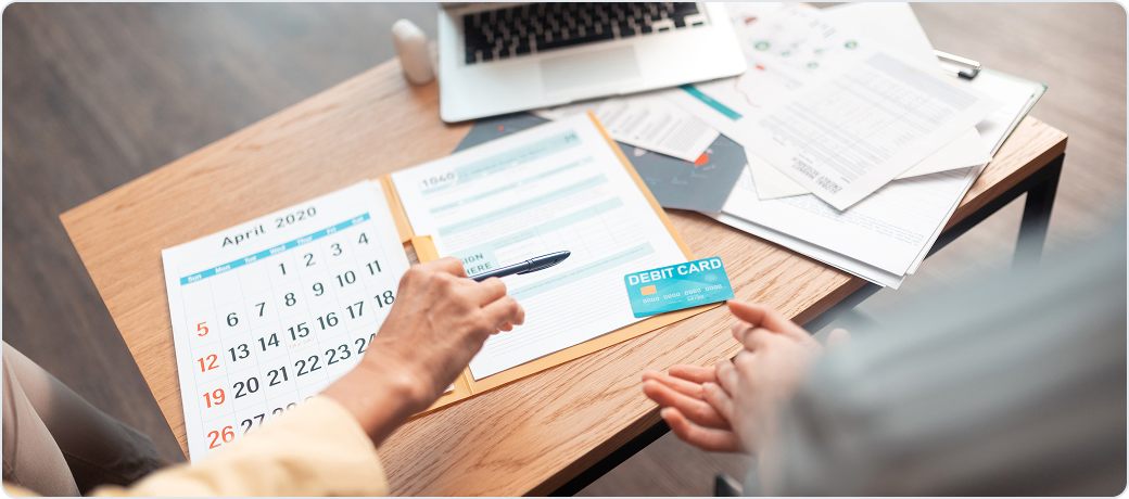 Calendar, tax form, debit card and bills spread across a desk