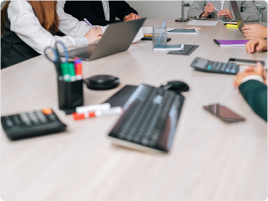 Team meeting around a conference table with laptops, calculators and notebooks